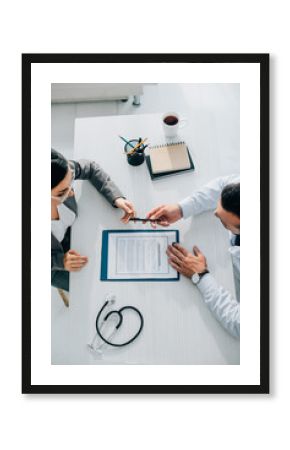 high angle view of doctor giving pen to patient to sign insurance claim form in clinic