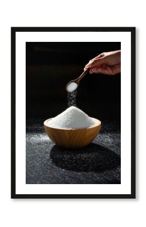 People are pouring sugar or salt with a wooden spoon to put in a wooden bowl. Black background.
