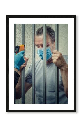 Temperature Screening of Masked Prisoner Through Bars with Infrared Thermometer Emphasizes Prison's Efforts to Prevent Viral Outbreaks.