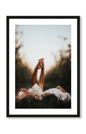 Young couple lying on grass, holding hands an looking at each other.