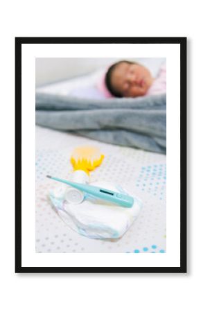 Close-up of a diaper and thermometer for newborn babies, with a blurred baby in the background in a vertical photo, showing child care and health