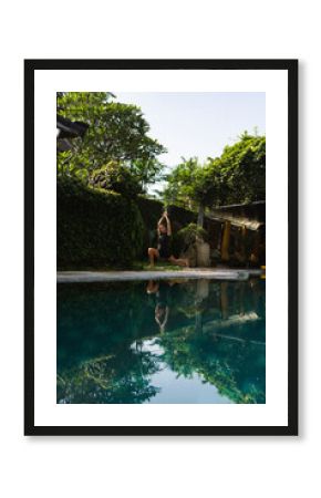 Woman practicing yoga beside serene tropical pool