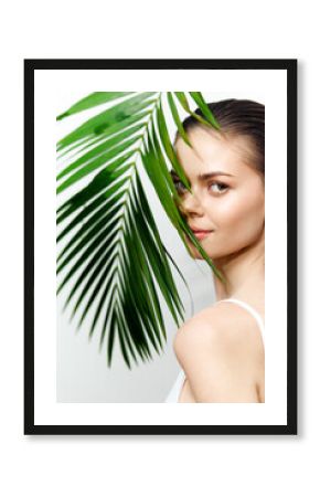 Young woman with palm leaf, showcasing natural beauty and serene expression against a clean, minimal background. Perfect for wellness and skincare themes.