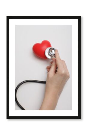 Hand holding stethoscope checking red heart on white background, symbolizing cardiology, healthcare, heart disease prevention, and medical diagnostics. Concept of heart health, love, and wellness.