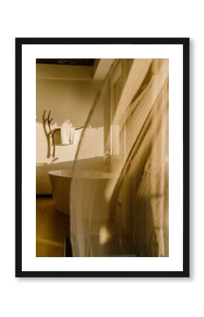 A luxurious bathroom with a freestanding bathtub, bathed in warm golden sunlight. A large window offers a breathtaking ocean view, blending modern elegance with a tropical, nature-inspired ambiance