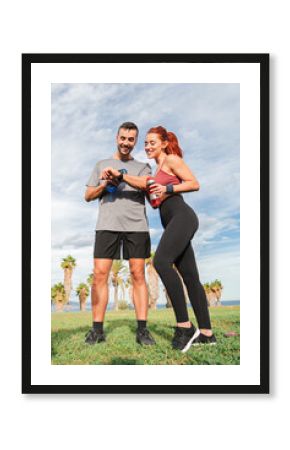 Energetic Couple Engaged in Checking Their Fitness Watches While Taking a Relaxing Break Together. Sharing Joy and Motivation, Embracing Their Active Lifestyle and Commitment to Health and Fitness