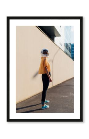 Young woman with space helmet standing by wall