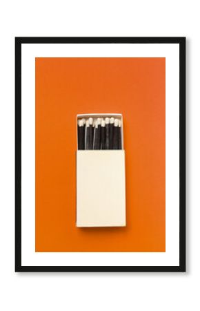 Black matches in a box on a orange background.