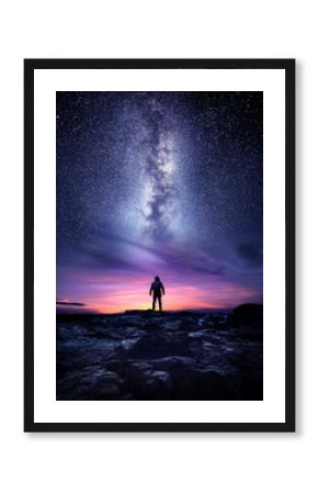 Night time long exposure landscape photography. A man standing in a high place looking up in wonder to the Milky Way galaxy, photo composite.