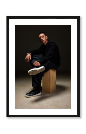 Young man sitting on wooden block in low light environment