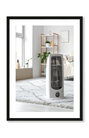 A modern white space heater stands on a light beige geometric rug in a bright room.