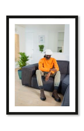 White VR headset resting on grey sectional sofa in living room with potted plant, copy space
