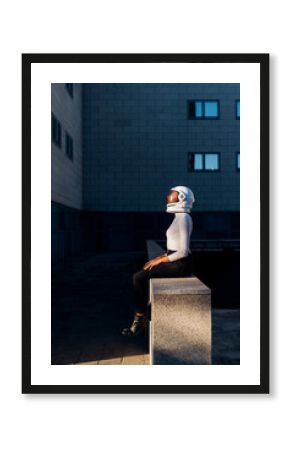 Businesswoman wearing space helmet sitting on wall by office building