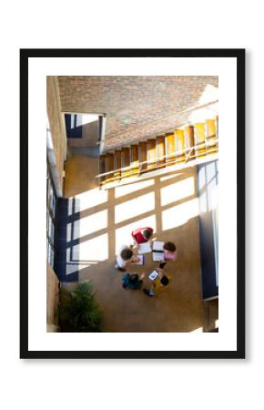 High angle of diverse creative colleagues using tablet and discussing in office corridor, copy space