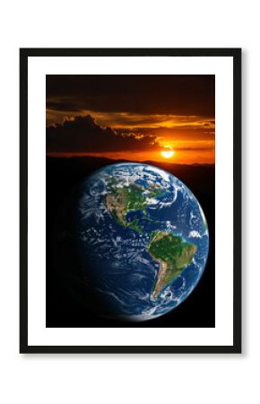 The planet Earth floats in space with a brilliant orange sunset and dark clouds behind mountains on the horizon, evoking nature's majesty