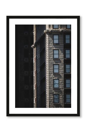 View of light playing on the textured facade of a tall building with evenly spaced windows, casting shadows on the adjacent dark structure, New York, New York, United States.