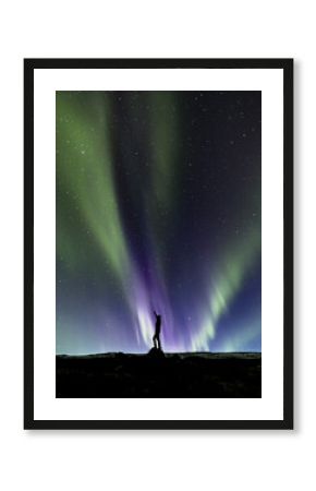 View of a lone silhouette reaching up at the ethereal dance of the aurora borealis, painting the night sky with vibrant greens and purples, Reykjavík, Aurora Borealis, Iceland.