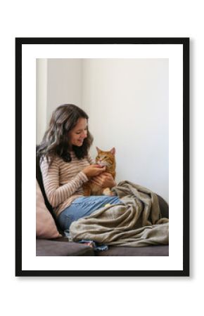 Brunette young woman playing with her rescue red cat at home. Copy space background.