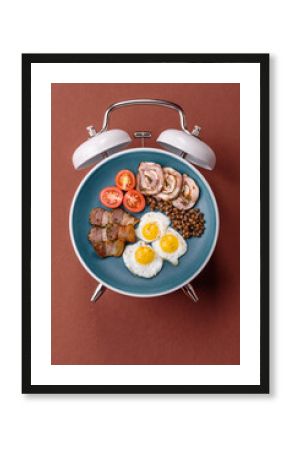 Breakfast of fried eggs with bacon or sausage and vegetables. ? plate on a vintage alarm clock