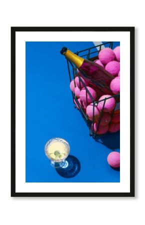 Champagne bottle with pink tennis balls and crystal glass on blue court. Concept of premium leisure, branding for sport events, lifestyle editorial and beverage advertising.