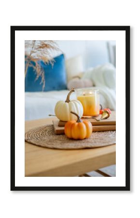 Home autumn decor in warm shades. Pumpkin, candle, dried flowers, pillows.