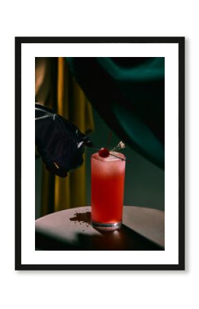 Red cocktail with cherry garnish and black glove hand on table. Concept of premium alcohol branding, stylish event posters, and creative beverage advertising.