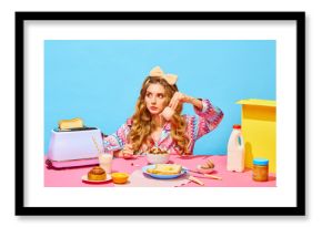 Food pop art photography. Sad young girl with long curly hair preparing milk flakes with hungry eyes over light blue background. Table with milk, butter, bread