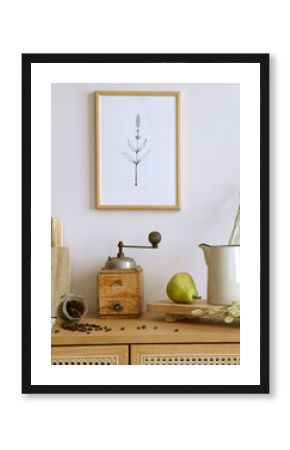 Creative composition of kitchen space with mock up poster frame, rattan commode, pears, mill, food, boho basket and kitchen accessories. Home decor. Template.