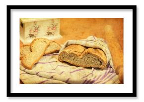 Homemade bread wrapped in a dish towel, two bread slices next to it, and a rolling pin. Gorgeous decoupage box is partially visible. Vintage look added in post processing. Selective focus.