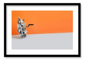 Comical robotic toy waiter with an empty tray in his hand. The concept of a technological artificial intelligence staff in the restaurant business. orange gray background, blank space