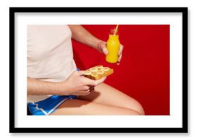 Drink and snack. Female body with male hands holding toasts with banana and orange juice over red background. Vintage, retro style.