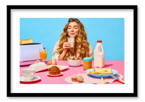 Food pop art photography. Happy beautiful young girl with ginger hair drinking milk over light blue background. Table setting for breakfast