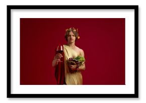 Young man in toga holding grapes and red wine glass on festive background. Concept of vineyard lifestyle, restaurant promotion, drink campaigns, and advertising visuals.