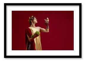 Young man in toga holding grapes and antique jug with proud look. Concept of restaurant branding, healthy lifestyle promotion, food photography, and social media visuals.