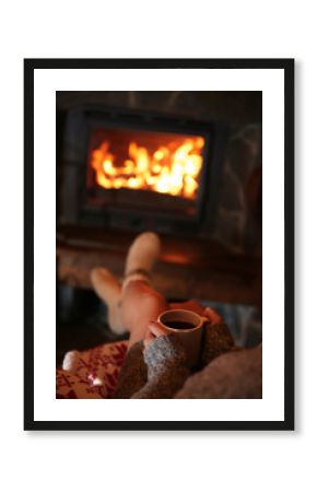 Woman resting with cup of hot drink near fireplace