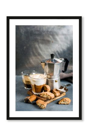 Glass of latte coffee on rustic wooden board, cantucci biscuits and steel Italian Moka pot, grey background