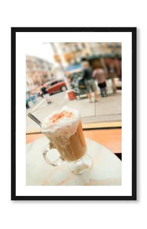 Frothy mug of cappuccino at coffee house with urban scene outside window