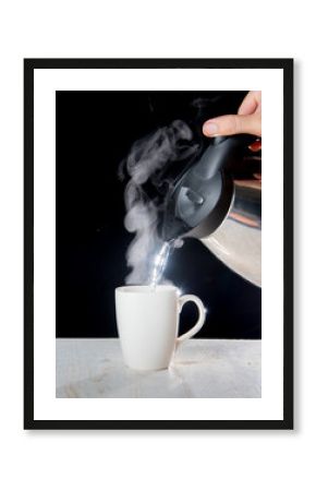 kettle pouring boiling water into a cup with smoke on wood table