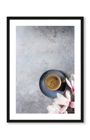 Blue cup of black espresso coffee and spring flowers magnolia branches over grey texture background. Top view, copy space. Spring greeting card