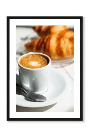 Hot coffee and croissant breakfast in a sunny morning, natural light.