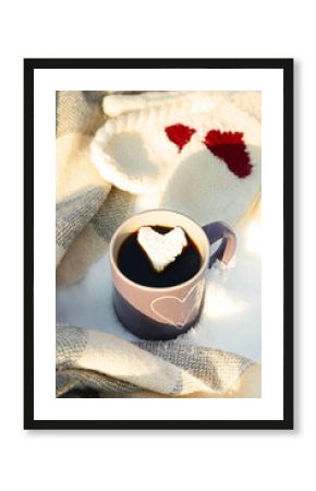 Cup of hot coffee with heart marshmallow and warm clothes on snowy background, close up