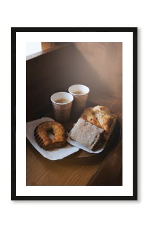 Fresh sweet bakery bread, two kraft cups of black coffee on a paper tray, wooden background. Coffee break concept. Breakfast in the sunny morning