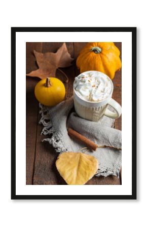Spicy pumpkin latte with cinnamon and autumn leaves on wooden background