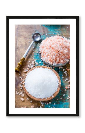 Two different types of natural salt in stone bowls on wooden surface. White sea salt, pink Himalayan salt