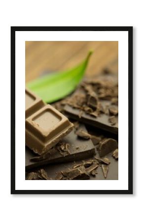 milk chocolate square is resting on dark chocolate fragments beside green leaf in macro photography