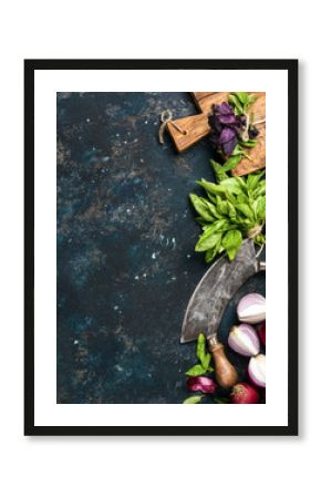 Healthy food cooking background. Fresh green and purple basil leaves, red onions and garlic, herb chopper knife and rustic cutting board over grunge dark blue plywood texture. Top view, copy space