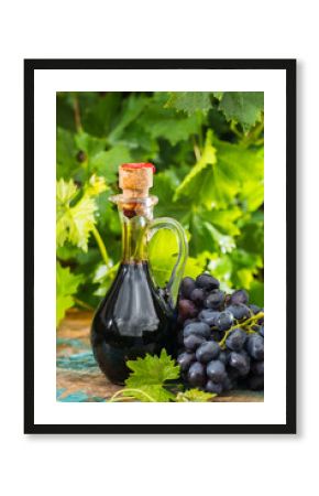 Black old balsamic vinegar in a glass jug with fresh red grapes on green vineyard background