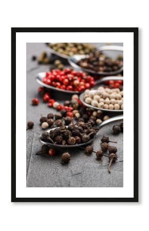 Colorful peppers in spoon on black table - cubeb, pink, green and white closeup. Spices. Selective focus