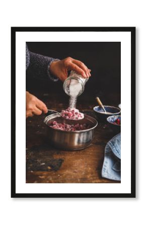 Red berries jam. Person making jam, jelly, confiture over rustic wooden table.