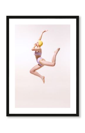 Portrait of young woman in swimming suit and cap jumping into water isolated on grey studio background. Summer activity.